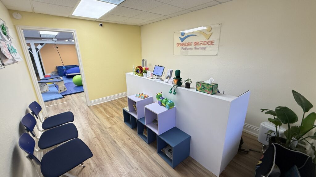 Sensory Bridge reception area with the clinic sign, seating, and a view into the therapy gym.