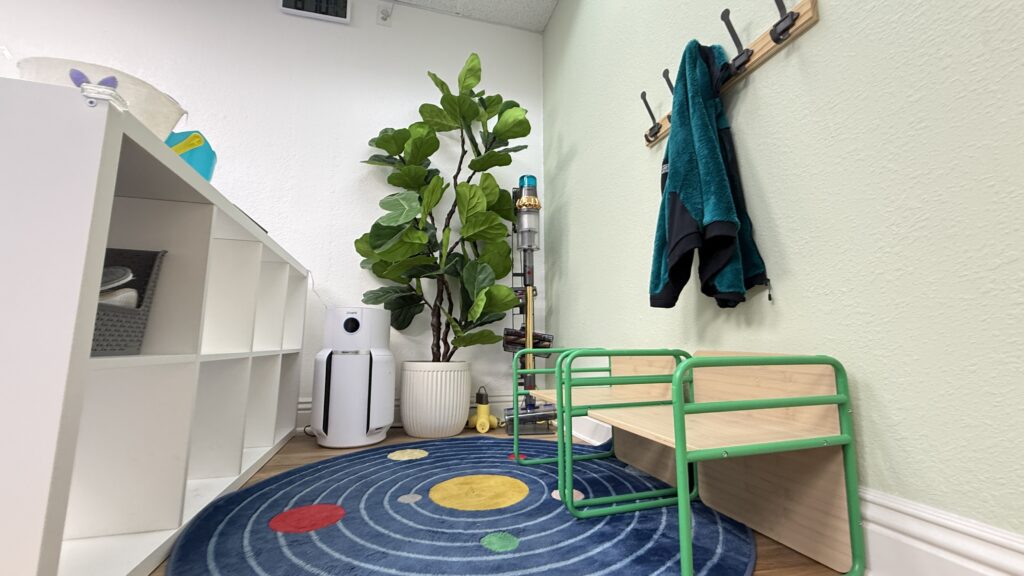 Small seating area with green-framed stools, white storage cubbies, and a plant.