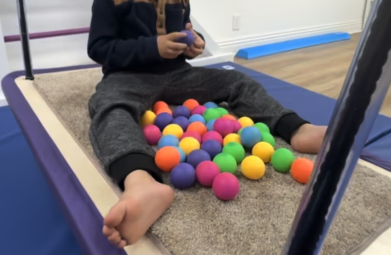 Child seated on a platform swing with colorful balls.
